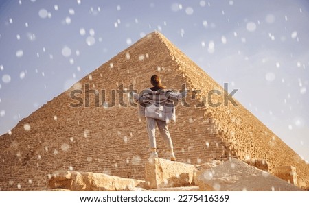 Concept anomalous cold cyclone, climate change. Winter snow on background of Pyramids of Cheops Egypt tourist girl in warm jacket. Royalty-Free Stock Photo #2275416369