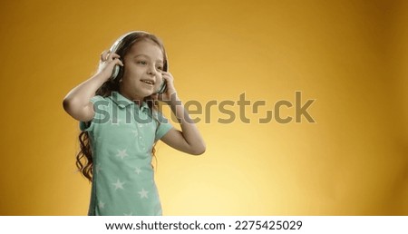 Copy space. Funny caucasian girl in casual clothes cap posing isolated on yellow background studio portrait. People lifestyle concept. Mock up copy space. Listening music with headphones, dancing