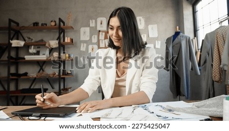Asian female clothing designer is drawing her sketches on graphics tablet, preparing her new collection - fashion, success concept 