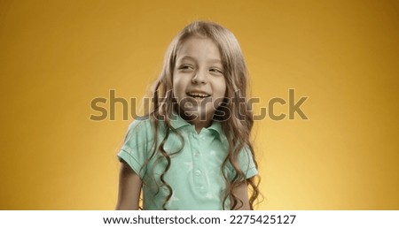 Little caucasian girl looking at camera and bursting into laughter, expressing positive emotions, isolated on yellow background - emotions concept close up 