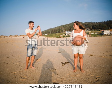 Pregnant couple in the beach. Man is taking a photo to the woman