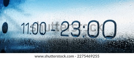 Opening time hours images on wet glass of building door. Service and working time concept.