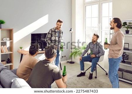 The company of young bearded best friends talking and laughing at home with a bottle of beer in their hands. Happy smiling men communicating with each other indoors. The concept of friendship. Royalty-Free Stock Photo #2275487433