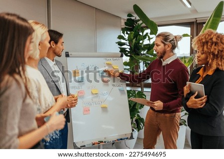 A young Caucasian businessman is presenting a chart on a whiteboard to his team in a business meeting in the conference room. Royalty-Free Stock Photo #2275494695