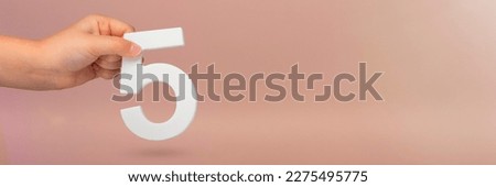 Number five in hand. Hand holding white number 5 on red background with copy space. Concept with number five. Birthday 5 years, fifth grade, five day work week Royalty-Free Stock Photo #2275495775
