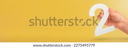 Number two in hand. Hand holding white number 2 on yellow background with copy space. Concept with number two. 2 percent, birthday 2 years old, couple, two, double Royalty-Free Stock Photo #2275495779