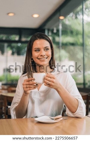 Vertical social media format photo of a Caucasian woman holding a cup of coffee. Concept of a person drinking coffee. Beautiful young woman sitting in a coffee shop