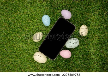Phone with blank empty screen on background of easter eggs with  in  on green grass. Space for text. Happy Easter! Smartphone mockup, top view
