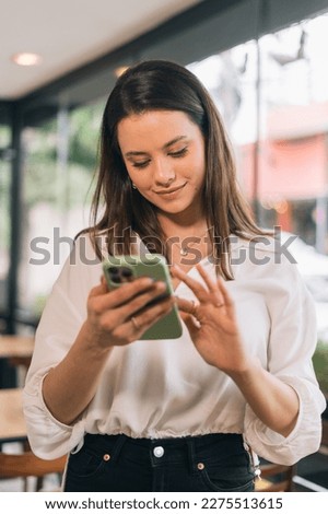 Networking format, portrait photo of Hispanic businesswoman in formal attire in her office happy and cheerful while using smartphones and working. Young businesswoman using apps on cell phones, readin