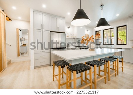 Modern farmhouse kitchen interior with light wood floors white granite marble counters large dining table with eight chairs stainless appliances orange color accents and large windows with black trim Royalty-Free Stock Photo #2275521117