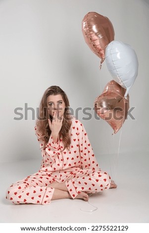 a girl in pajamas with a heart print and three gel balls in the shape of a heart. Valentine's day. blonde girl on a white background and pink and white gel balls. pajama party clothes for sleep 