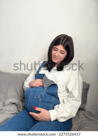 Peaceful pregnant woman touching big 9 month belly in light interior of kids room, feeling kicks, stroking baby bump, calming unborn child. Expectation, pregnancy concept