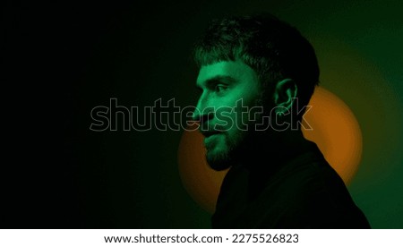 Side view artistic creative portrait of man looking away in orange neon lights on dark green background. Modern photo handsome bearded middle age man with earringsin the ear. Copy space. Banner