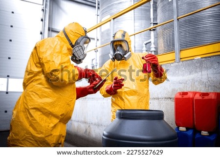 Quality control workers in protective suit and gas masks sampling chemicals in production plant. Royalty-Free Stock Photo #2275527629