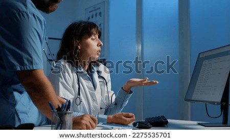 Medical staff looking at computer monitor analyzing patient report while discussing medication treatment to help cure disease. Physician and nurse working night shift in hospital office