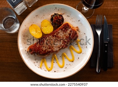 hot baked entrecote with vegetables decorated with onion rings is served in baking dish Royalty-Free Stock Photo #2275540937