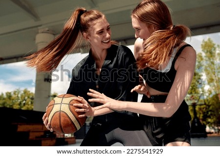 Two young women playing basketball on street court on a sunny day. Women playing a streetball game outdoors.