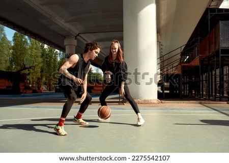 Athletic young people play streetball on the street, a girl and a guy play basketball on the city playground.