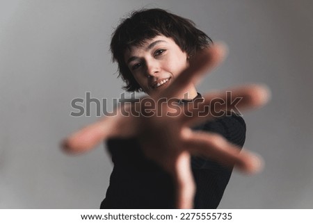 Blurred foreground. Woman reaching forward with her hand. Medium shot. Grey background. High quality photo Royalty-Free Stock Photo #2275555735
