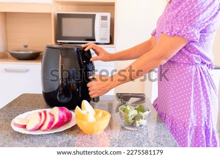 Brazilian woman using air fryer to fry food in home kitchen. Electric fryer without oil Royalty-Free Stock Photo #2275581179