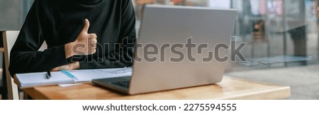 Smiling female student studying on laptop while sitting in cafe and showing thumb up