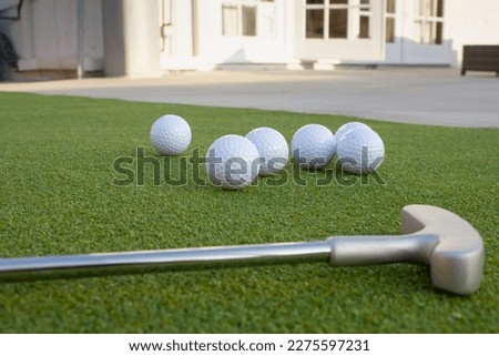 A ground level closeup view of several golf balls and putter, in a backyard putting green setting. Royalty-Free Stock Photo #2275597231