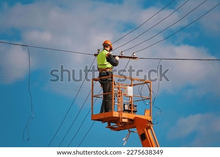 Man repair broken electric cable at height. Man in hardhat repair damaged wire on truck crane. Worker in lift bucket repair power line. Electrician worker in crane cradle repairs electrical wires. Royalty-Free Stock Photo #2275638349