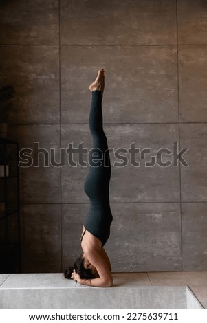 Young sporty attractive woman practicing yoga, doing headstand exercise, variation of salamba sirsasana pose, working out, wearing sportswear, grey top, indoor close up view, yoga studio, rear view Royalty-Free Stock Photo #2275639711