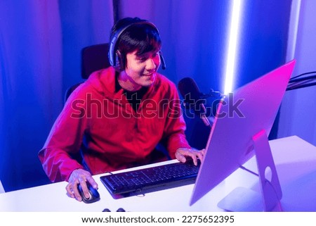 Professional gamer casting podcast walkthrough review. Young asian man sitting on chair with computer pc and microphone. Happy male Streamer wearing headphone playing game online in room neon light Royalty-Free Stock Photo #2275652395