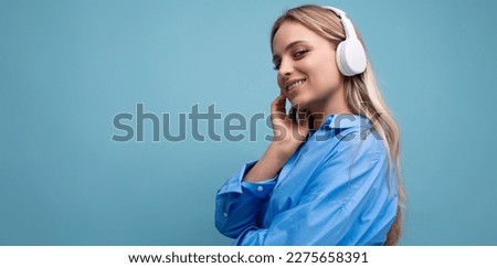 horizontal photo of an attractive girl in wireless large headphones listening with pleasure to music from a playlist on a blue background