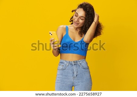 Influencer woman with phone in hand taking selfies talking on video call freelancer social media technology work, with curly afro hair in blue shirt yellow background , smile with teeth, copy space