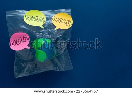 Earth Day. Globe enclosed in a plastic bag on blue background with HELP messages. Copy space.