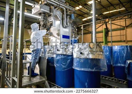 A worker controls an automatic aseptic filling machine filling ketchup into large drums at an industrial plant. food industry. Agriculture industry. Royalty-Free Stock Photo #2275666327