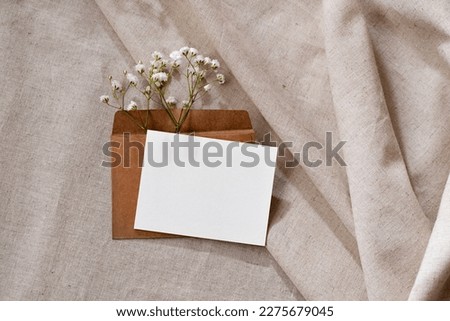 Empty paper card with mockup copy space, envelope with flowers on a neutral beige linen background, elegant aesthetic business brand template, advertising, invitation or greeting card