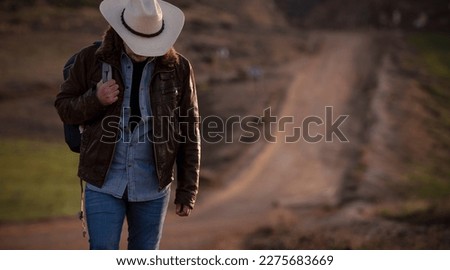 Adult man in cowboy hat walking on dirt road against sky during sunrise Royalty-Free Stock Photo #2275683669