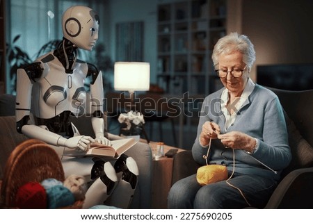 Elderly woman knitting on a sofa with her companion android reading a book in the living room. Concept of elderly care and future. Royalty-Free Stock Photo #2275690205