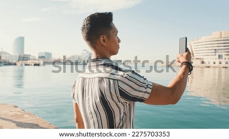 Close up, young man stands on the pier and takes photo on mobile phone