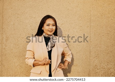 Smiling Asian businesswoman standing against the wall and looking at camera. Copy space.