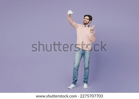 Full body young IT man wear casual clothes pink sweater glasses doing selfie shot on mobile cell phone post photo on social network show v-sign isolated on plain pastel light purple background studio