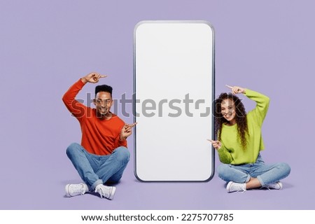 Full body young couple two friends family man woman wear casual clothes together point finger on big huge blank screen mobile cell phone with area r isolated on pastel plain light purple background