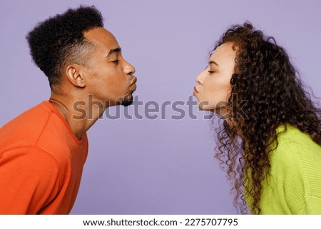 Side view young couple two friends family man woman of African American ethnicity wear casual clothes together kiss each other with closed eyes stand face to face isolated on plain purple background Royalty-Free Stock Photo #2275707795
