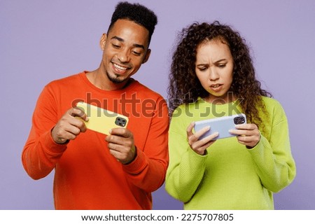 Young couple two friends family man woman of African American ethnicity wear casual clothes together using play racing app on mobile cell phone gadget isolated on pastel plain light purple background
