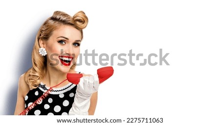 Portrait image - happy smiling beautiful woman hold red phone tube, in pin-up black dress with gloves, isolated over white background. Pinup blond girl. Wide composition photo