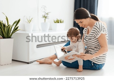 mother and daughter at home on the couch leafing through and looking a book with photos from a family photo shoot with a newborn baby. memory of important moments of life in the photo album. Royalty-Free Stock Photo #2275713925