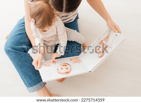 mother and daughter watch photobook from discharge of newborn baby.family tradition of printing photos and looking at them with children and remembering. Royalty-Free Stock Photo #2275714359