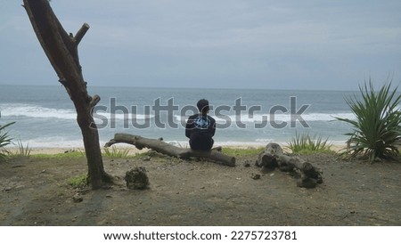 A man sit on the beach with a fallen tree trunk with a horizon line at the end of the beach