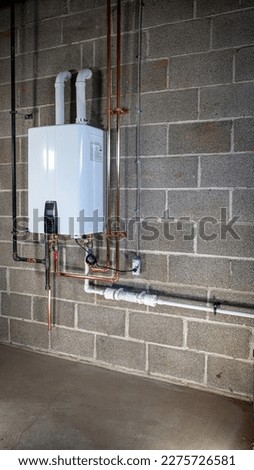 Installation of a tankless water heater. A professional installation a tankless water heater. A licensed plumber installed a new tankless water heater on a block basement wall. Royalty-Free Stock Photo #2275726581