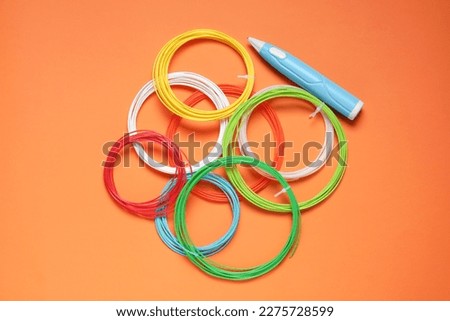 Stylish 3D pen and colorful plastic filaments on orange background, flat lay
