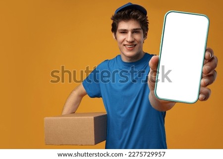Young delivery man showing smartphone with blank screen in studio