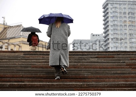 Woman with umbrella walking up the steps on city buildings background. Rain in spring city